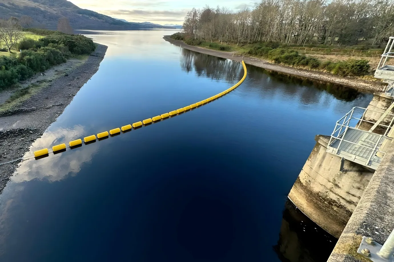 HDPE boom floating on a calm river near a dam, showcasing durability and flexibility compared to steel and PVC floating barriers – HDPE Boom vs Steel vs PVC.