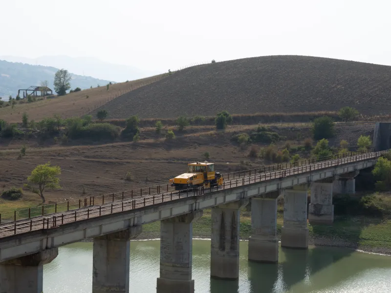 Ballast regulator machine traveling on a railway bridge for track maintenance.