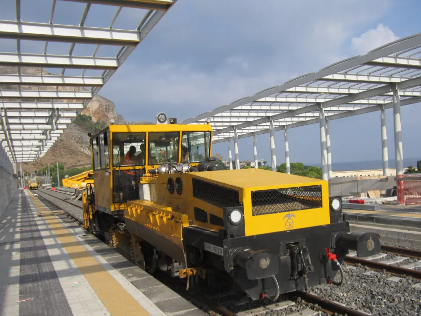 Yellow ballast maintenance equipment on railway tracks beside a station platform.