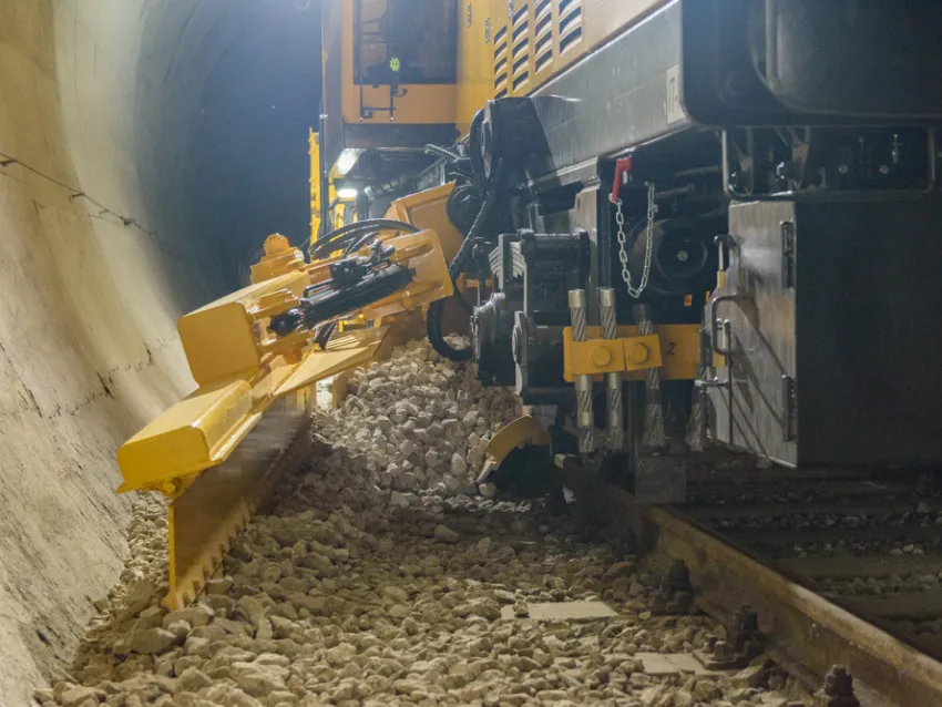 Ballast regulator arm shaping railway ballast inside a tunnel during track maintenance.