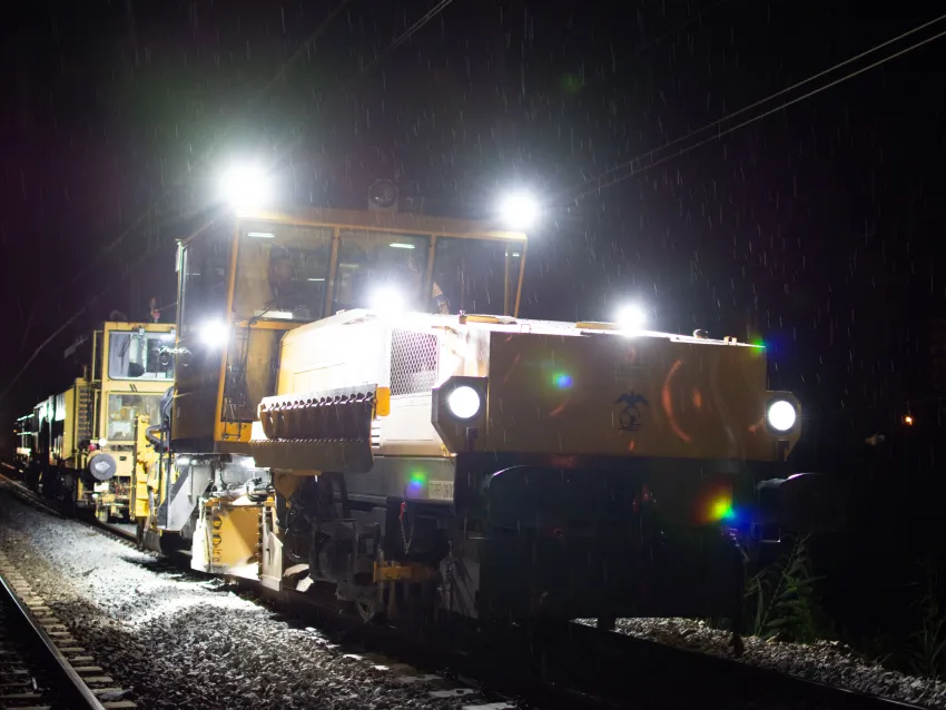 Ballast regulator machine working at night on railway tracks for ballast maintenance.