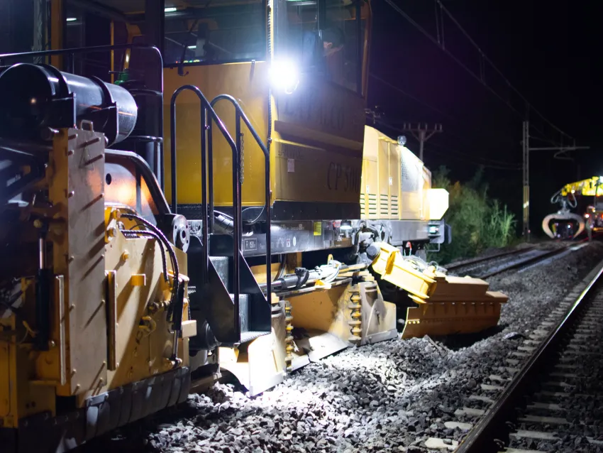 Ballast regulator equipment operating at night on railway tracks for ballast maintenance.