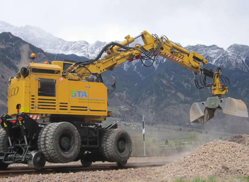 Rail excavator handling ballast beside railway tracks for maintenance work