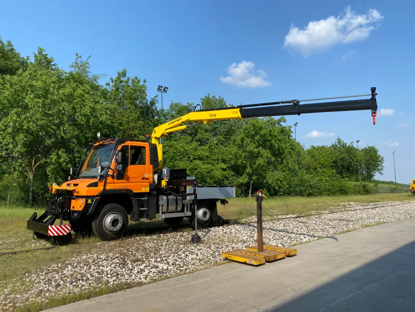 Hi rail truck with mounted crane operating beside railway tracks for maintenance work.