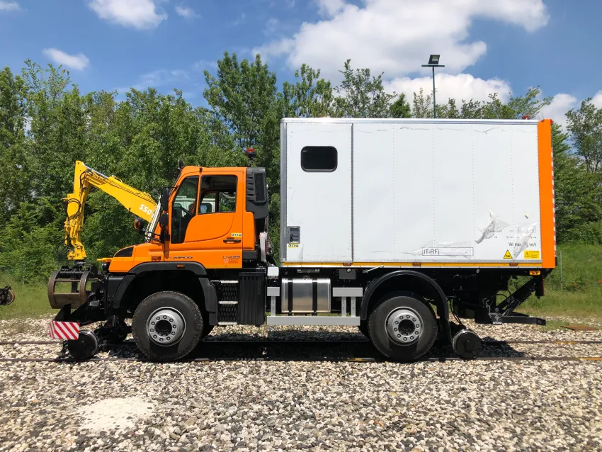 Hi rail truck with mounted crane on railway tracks for rail maintenance and trackside service work.