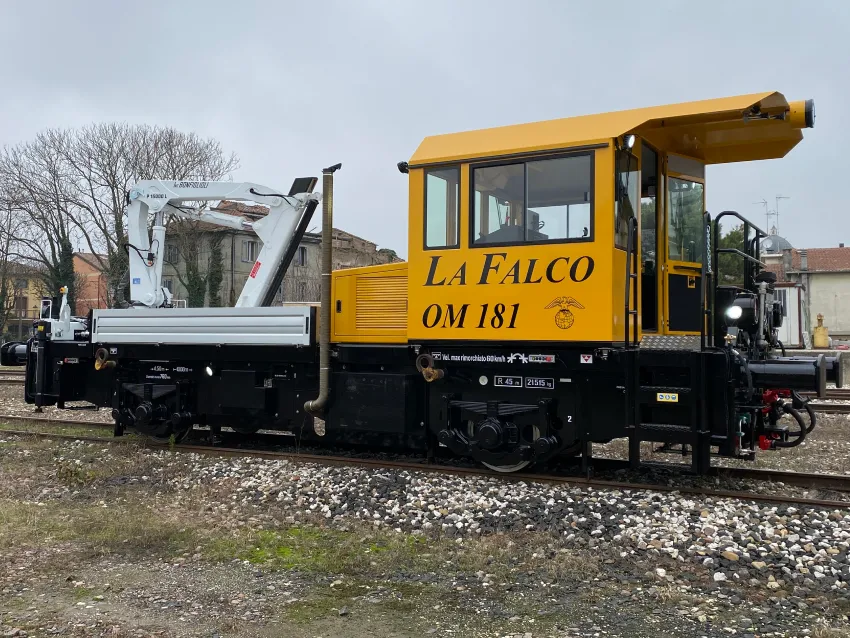 Industrial switcher locomotive on railway tracks with crane attachment for shunting and rail maintenance work.